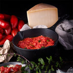 Vista en perspectiva del sartén profundo Victoria de 20 cm en hierro fundido esmaltado con capacidad de 1.9 litros con salsa de tomate, tomates frescos y queso sobre una mesa negra - Ferretería La Palma - 1050088