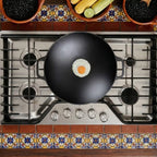 Vista cenital del sartén wok Victoria de 35.5 cm en hierro fundido esmaltado con un huevo frito sobre una estufa de gas en un ambiente de cocina tradicional - Ferretería La Palma - 1050038