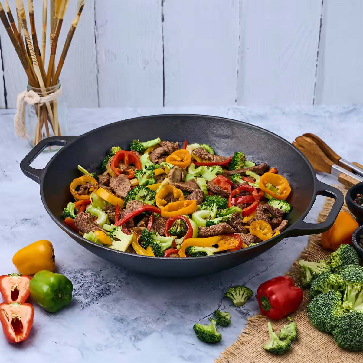 Sartén wok Victoria de 35.5 cm en hierro fundido esmaltado con un colorido salteado de carne, brócoli y pimientos sobre una superficie de mármol - Ferretería La Palma - 1050038