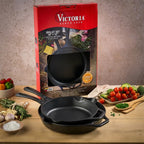 Vista del set de dos sartenes Victoria de 25 cm y 30 cm en hierro fundido esmaltado junto a su empaque original e ingredientes frescos sobre una mesa de madera - Ferretería La Palma - 1050150