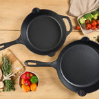 Vista cenital del set de dos sartenes Victoria de 25 cm y 30 cm en hierro fundido esmaltado rodeados de ingredientes frescos sobre una mesa de madera - Ferretería La Palma - 1050150