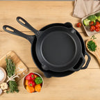 Vista cenital del set de dos sartenes Victoria de 25 cm y 30 cm en hierro fundido esmaltado apilados sobre una mesa de madera rodeados de ingredientes frescos - Ferretería La Palma - 1050150