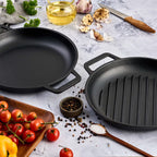 Vista en perspectiva del set de dos sartenes redondos Victoria de 25 cm en hierro fundido esmaltado con doble asa lateral, incluyendo un modelo liso y uno tipo grill, junto a ingredientes de cocina sobre una superficie de mármol - Ferretería La Palma - 1050149