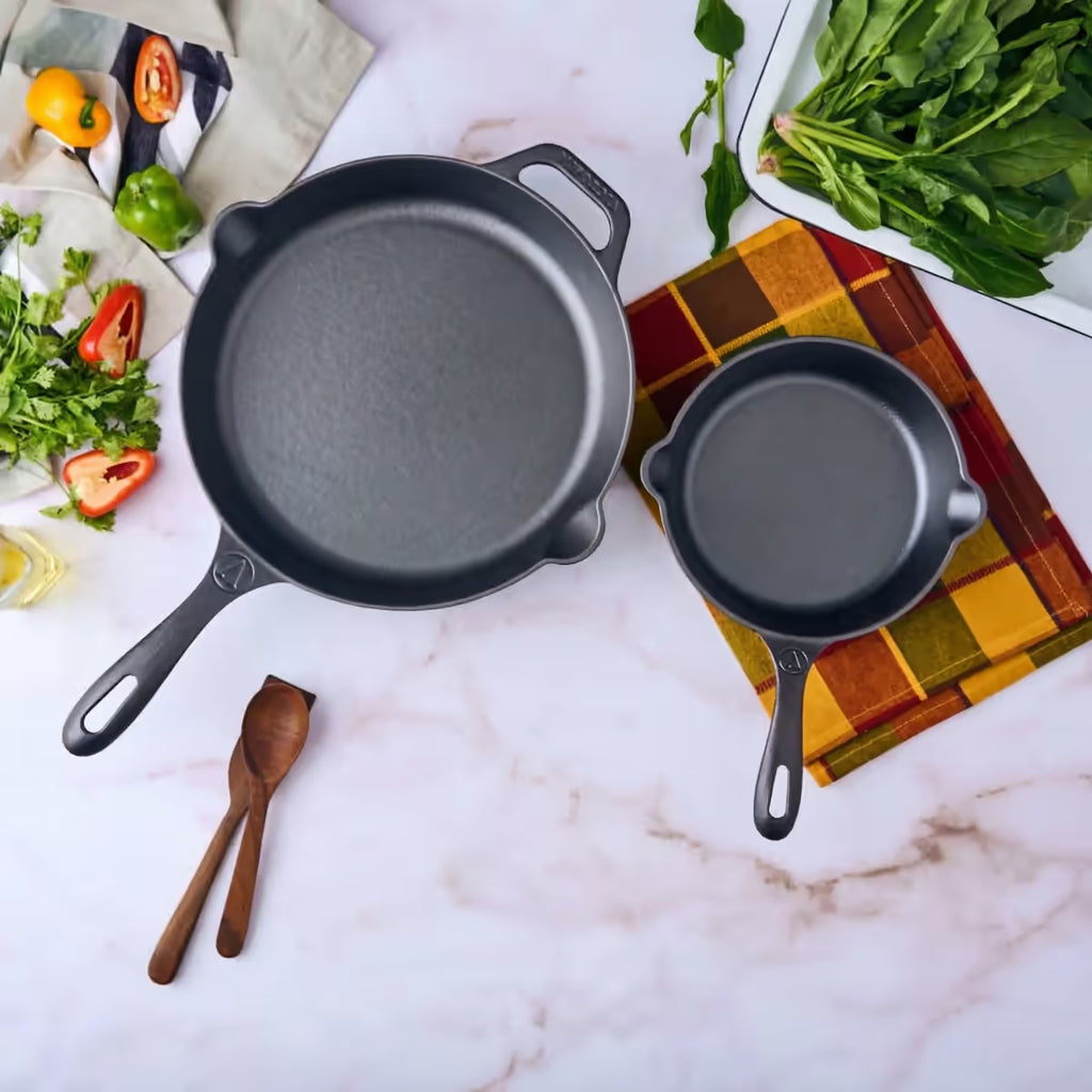 Vista cenital del set de dos sartenes Victoria de 20 cm y 25 cm en hierro fundido esmaltado rodeados de ingredientes frescos sobre una superficie de mármol - Ferretería La Palma - 1050099