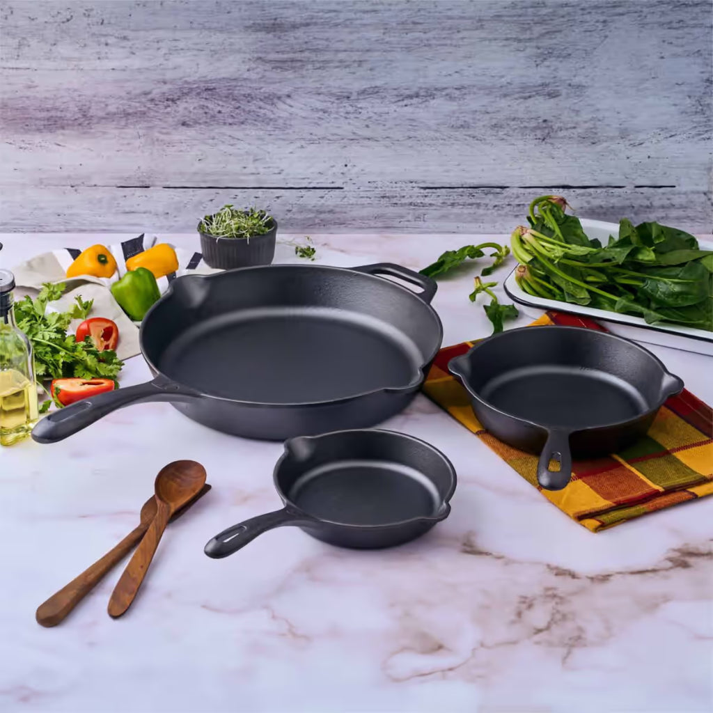 Vista del set de tres sartenes Victoria de 16.5 cm, 20 cm y 25 cm en hierro fundido esmaltado rodeados de ingredientes frescos sobre una superficie de mármol - Ferretería La Palma - 1050098