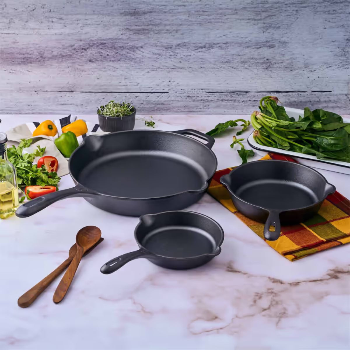 Vista del set de tres sartenes Victoria de 16.5 cm, 20 cm y 25 cm en hierro fundido esmaltado rodeados de ingredientes frescos sobre una superficie de mármol - Ferretería La Palma - 1050098