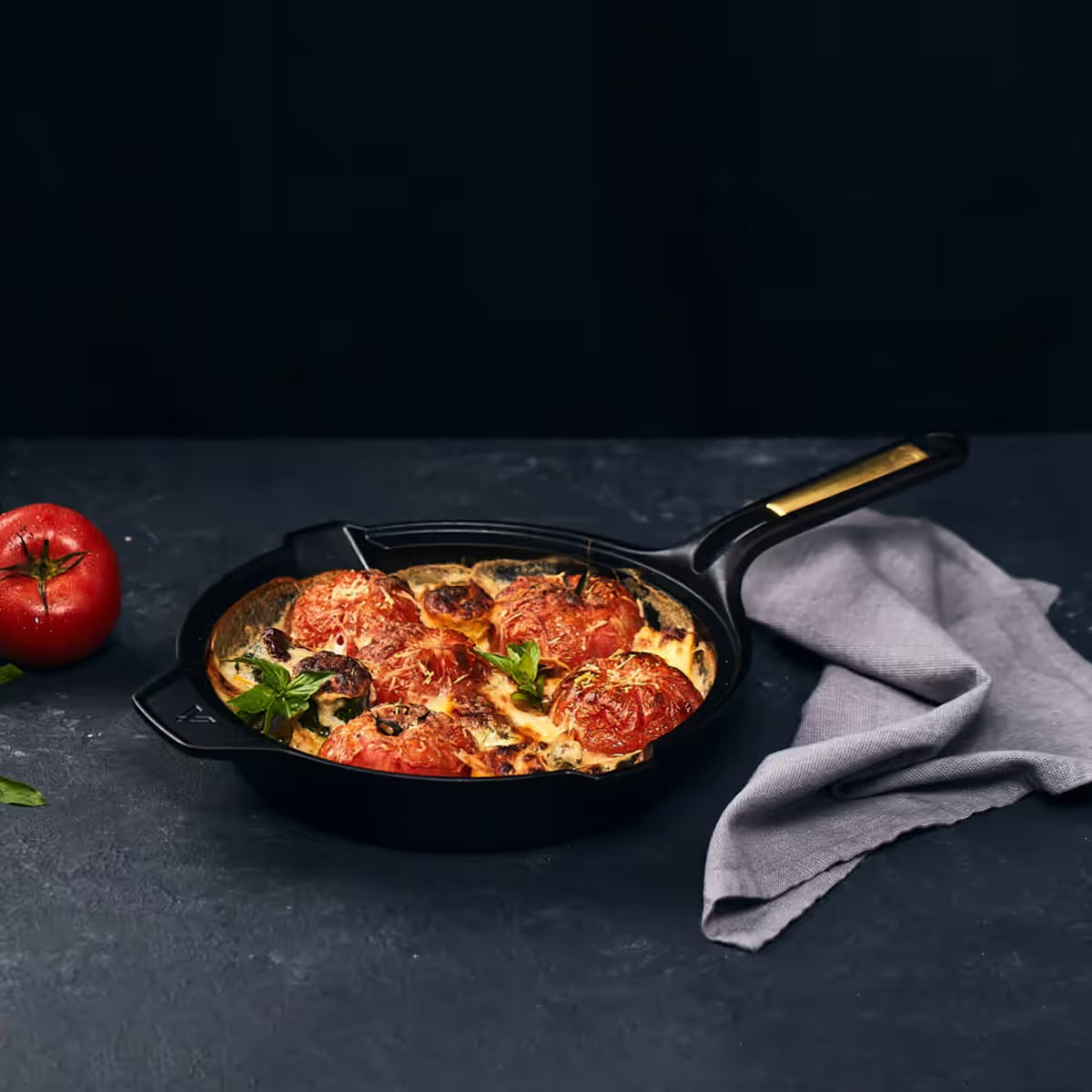 Sartén Victoria Signature 25 cm (10 pulgadas) con tomates horneados y queso gratinado sobre fondo oscuro y paño de cocina - Ferretería La Palma - 1050094